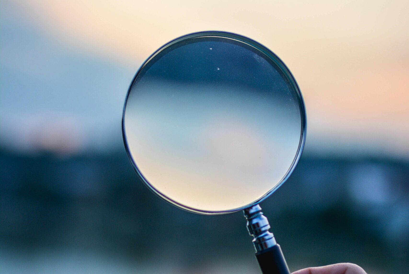 A magnifying glass held by a hand outdoors at sunset, focusing on exploration.